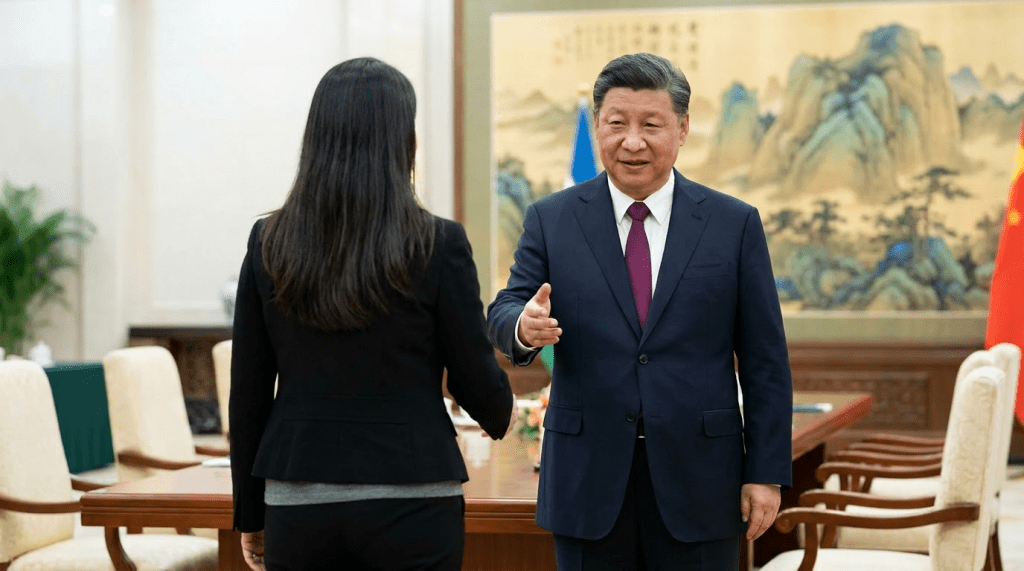 Two officials shaking hands in a formal setting with Chinese decor